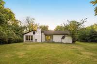 Back of the home opens to a wide outdoor space surrounded by greenery.