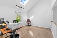 The loft area offers a bright and versatile space with an open view of the dining and family rooms below. A vaulted ceiling and skylight contribute to the spacious feel, while track lighting adds a clean, modern touch.