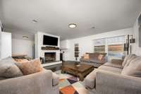 Spacious living room with a white brick fireplace, hardwood floors, and large windows for natural light.