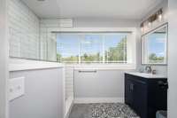 Updated secondary bathroom located off the flex room features patterned tile flooring, subway-tile shower surround, and a sleek navy vanity with modern lighting.