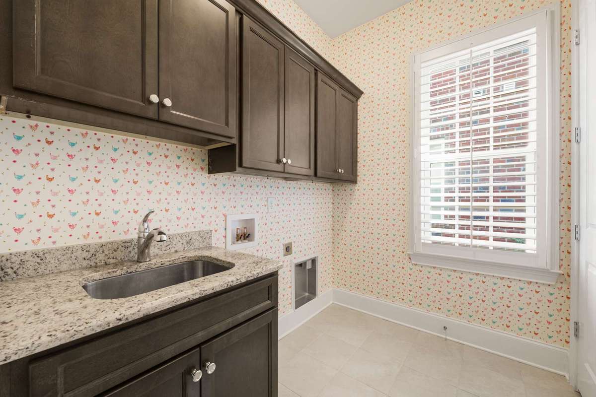 main floor laundry room offers extra cabinetry, utility sink, and extra storage / linen closet within.  Wall covering and plantation shutter added!