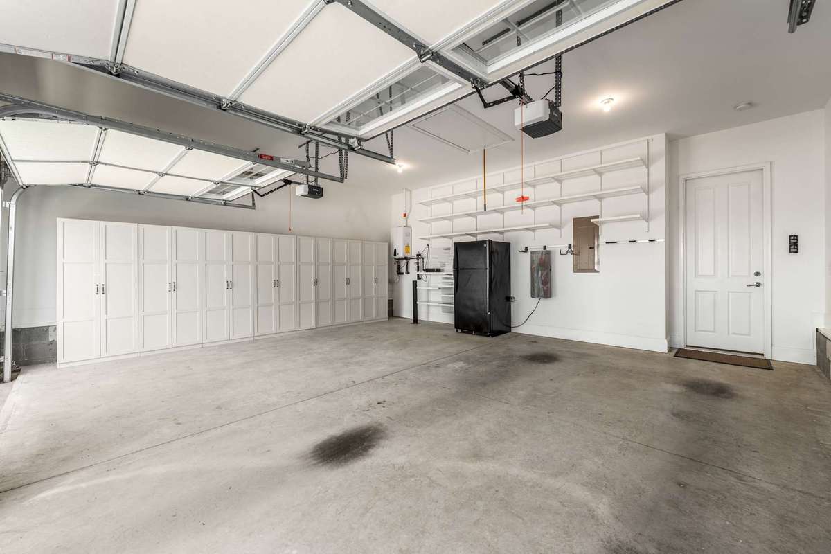 View of garage (no steps in) with storage shelving and cabinets added. Extra refrigerator. Gas tankless water heater. All convey