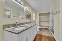 Bathroom featuring a double vanity with granite countertops, open shelving for convenient storage, and a spacious walk-in shower.
