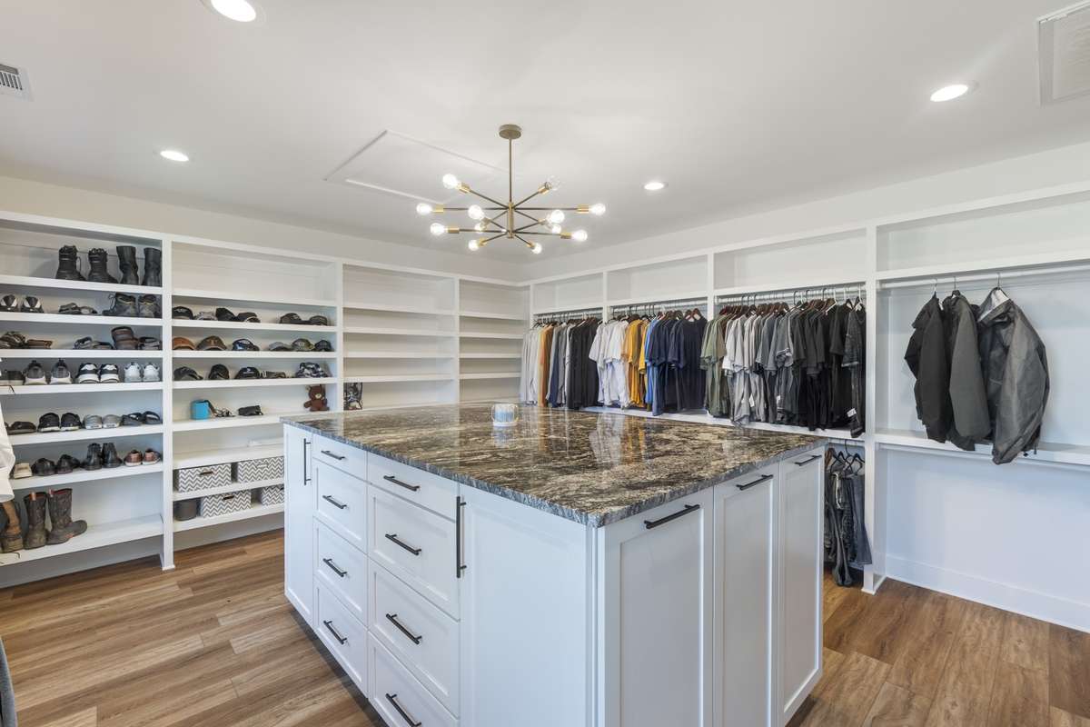 This custom built 16x19 closet room offers plenty of shelves, shoe racks, hanging space and even a custom island with drawers, cabinets and a granite countertop.