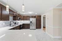 This beautifully renovated kitchen featuring quartz countertops, glass backsplash, rich espresso cabinetry, stacked-stone breakfast bar, contemporary pendant lighting and ceiling fan, tile floors & stainless steel appliances create a warm atmosphere.