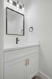 Half bath featuring quartz countertop with black & gold finishes just off garage entrance.