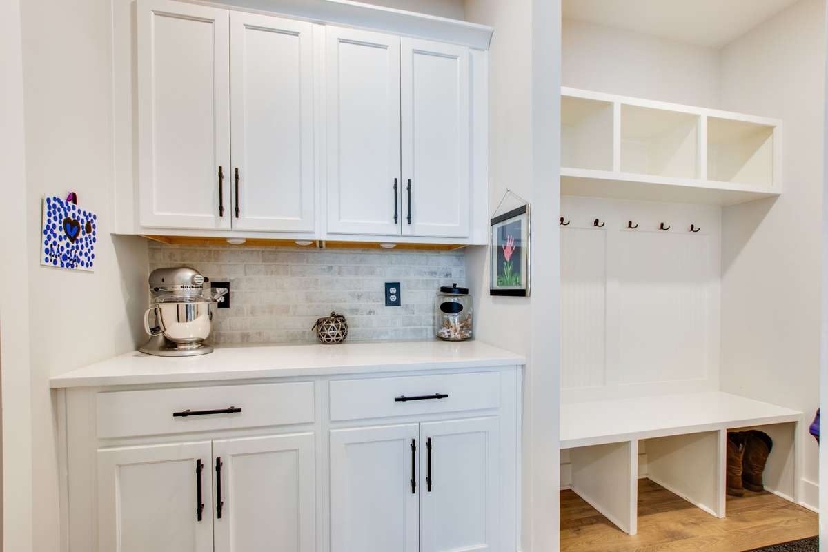 Mud room drop zone located as soon as you enter through the garage followed by the butlers pantry with full cabinets and the same brick tile backsplash...