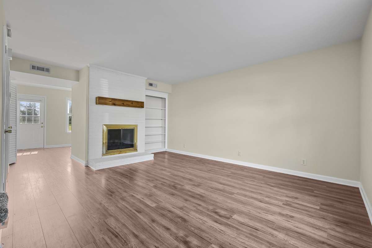 Spacious living room with warm laminate wood flooring, a wood burning fireplace, and built in bookcases for added character and function.