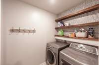 The laundry room is both functional and stylish, featuring a striking accent wall and custom shelving for organized storage and easy access to essentials.
