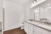 The classically white bathroom appeals with clean, clear lines and a crisp ambience, featuring a double vanity with granite countertops, undermount sinks, and brushed-nickel finishes.