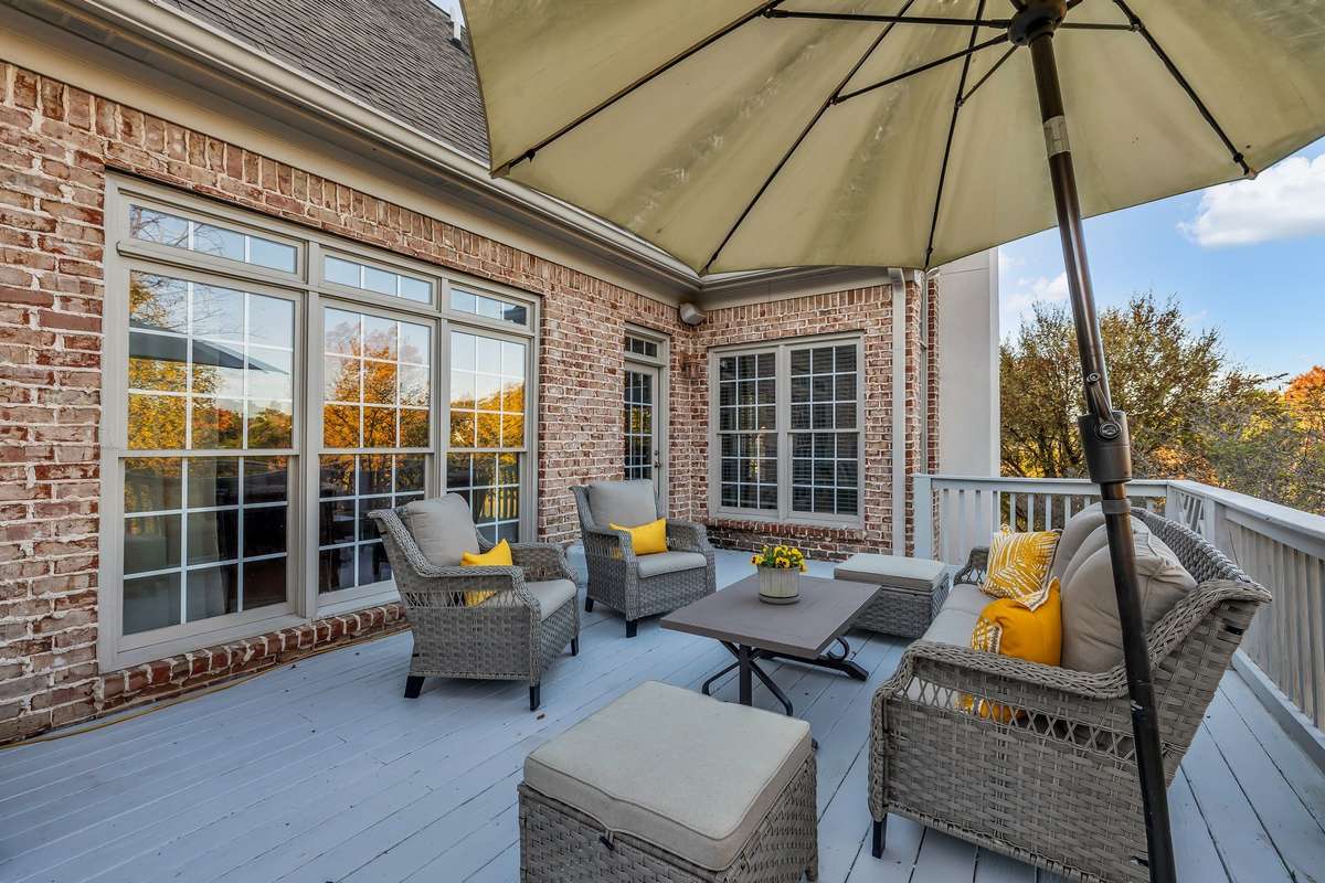 Spacious deck with room for lounging and dining, overlooking mature trees and open lawn.