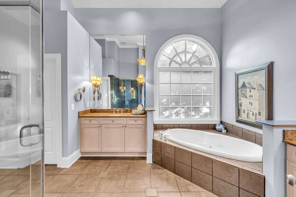 Spa-inspired primary bath with soaking tub, dual vanities, and arched window for natural light