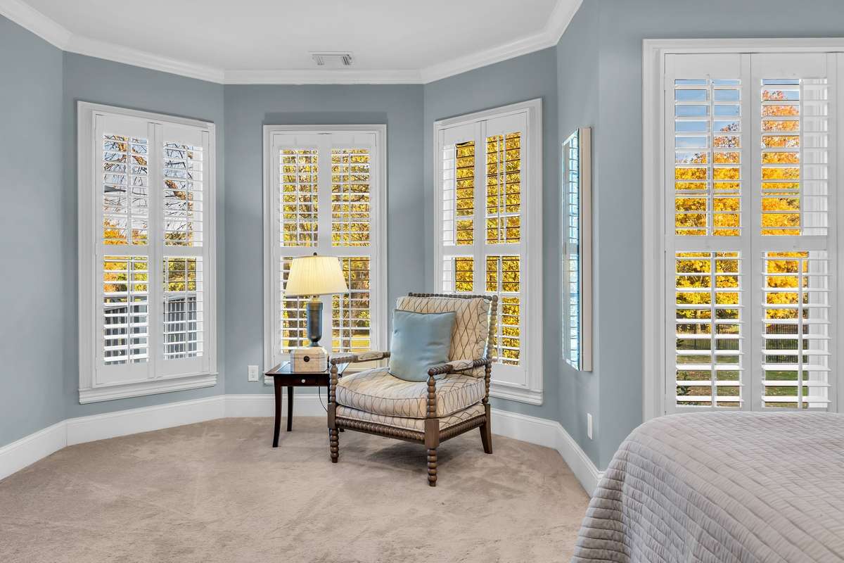 Serene bay-window sitting nook surrounded by plantation shutters and peaceful backyard views.