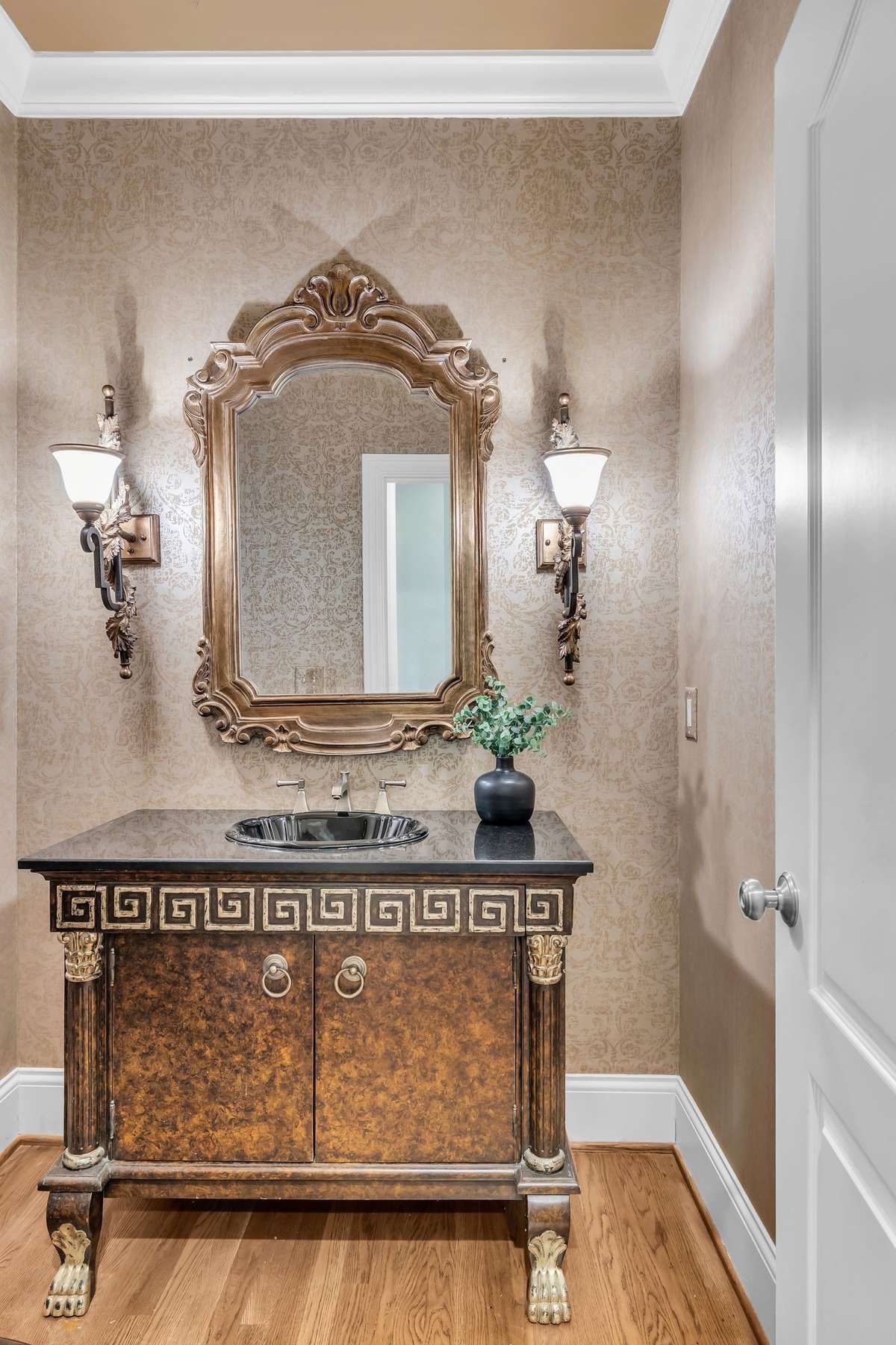 Elegant half bath with designer vanity, rich wallpaper, and sconce lighting.