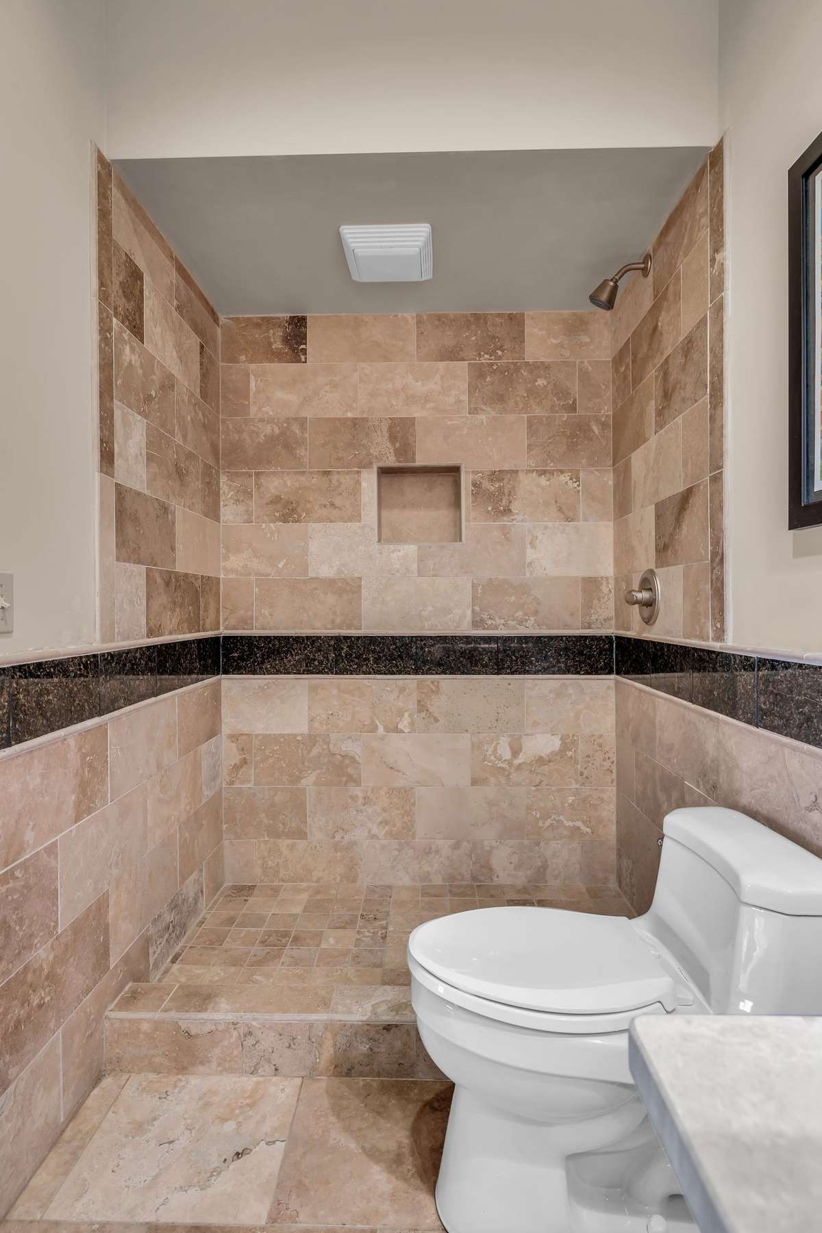 Spacious walk-in shower finished in travertine tile with elegant contrast trim.