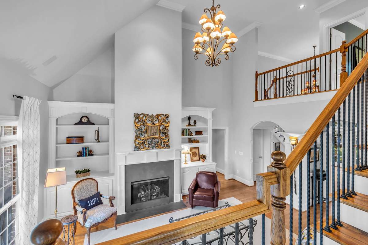 Dramatic two-story living room view highlights custom millwork, lighting, and open balcony overlook.