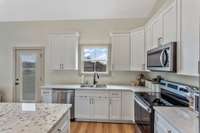 The kitchen features an oversized island with storage and ample room for seating, quartz countertops, stainless appliances, white shaker cabinetry with soft-close drawers.  Refrigerator, Range, Dishwasher, and Microwave-- all stay with the property!