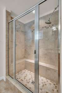 Nice tiled shower with bench in primary bedroom bathroom.