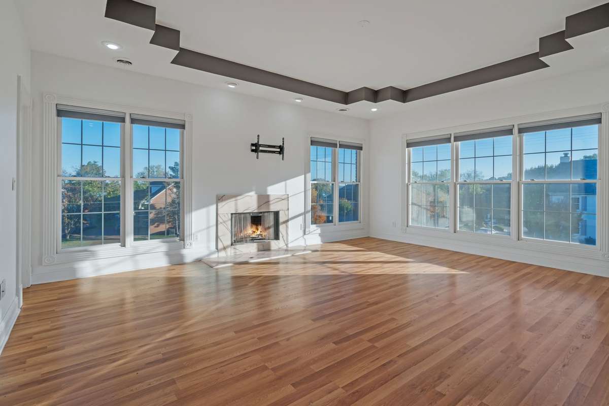 Another view of the sun-drenched primary bedroom with another fireplace and accented tray ceiling.