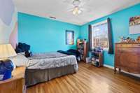 Bedroom with hardwood floors and a large window overlooking the yard. A colorful feature wall adds character and warmth.