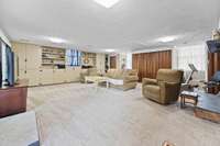 Spacious lower-level gathering room featuring fresh carpeting, wood accents, and a brick fireplace. Ample room for seating and storage.