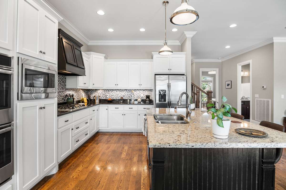 Chef's delight: a gas stove under a grand range hood with pot filler, double ovens, encased microwave, granite counters, & custom cabinets for seamless culinary creation.