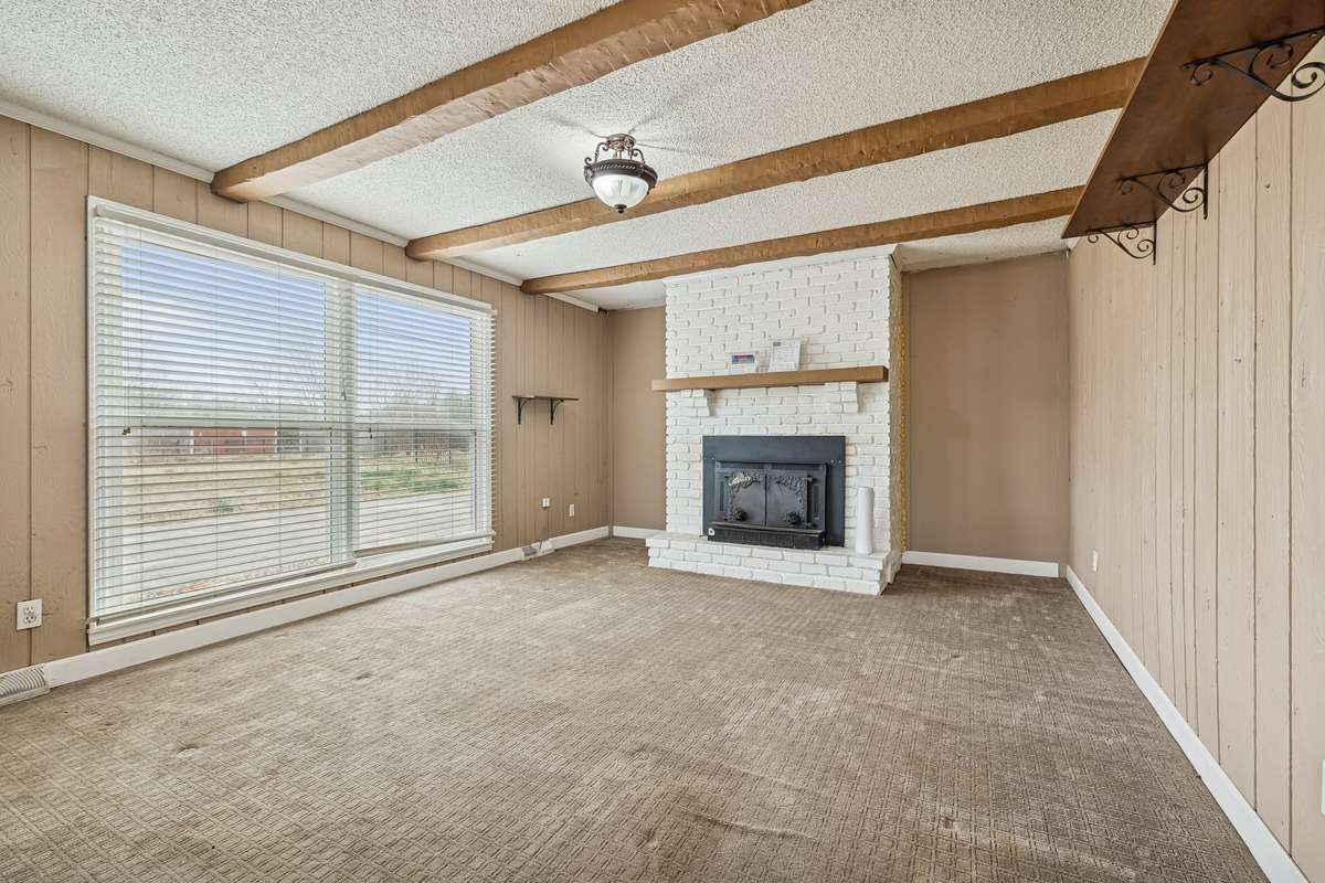 Spacious den with wood-burning fireplace, exposed beams, abundant natural light, scenic horse-farm views, and direct backyard access.