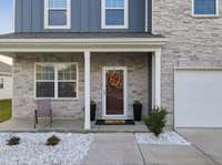 Inviting covered porch with fresh rock garden landscaping & freshly painted front door.