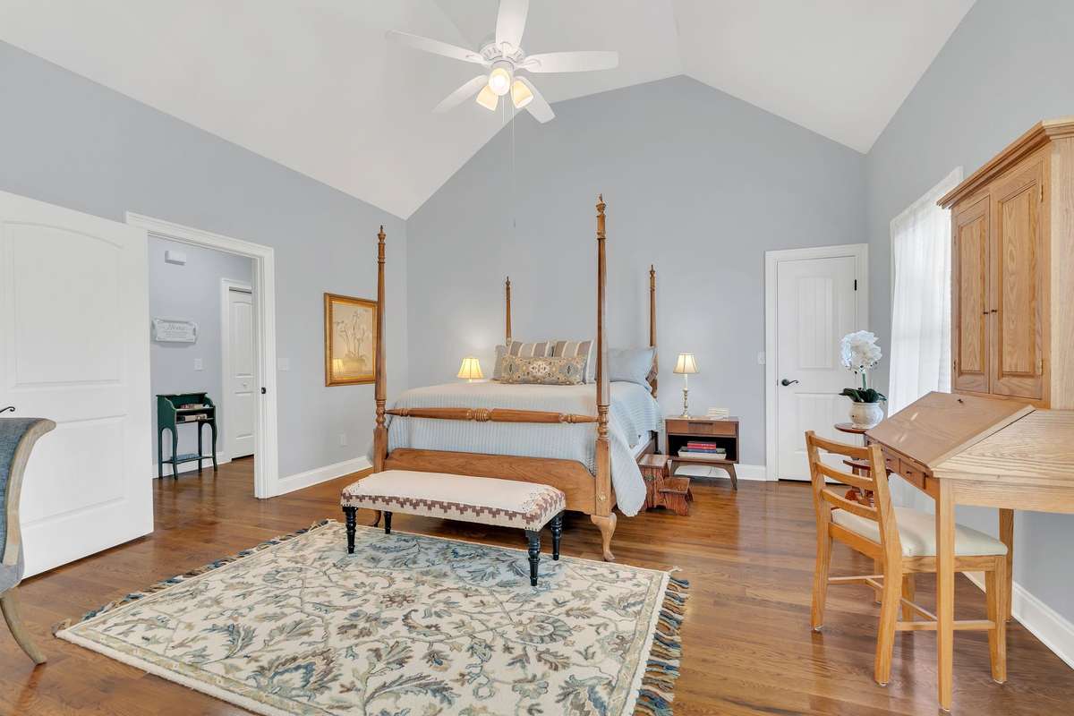 This view of the Primary Bedroom shows the vaulted ceiling, new ceiling fan and gleaming hardwood floors. The door opens to an "extra" closet.