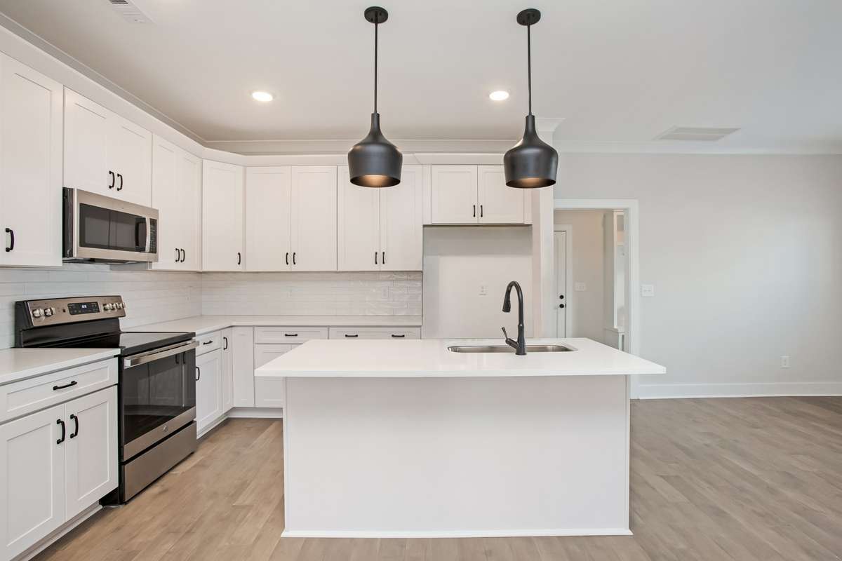 Picture is of the Madison Americana built on another lot Gorgeous kitchen featuring large island with quartz counter tops and pendant lights, tiled backsplash, stainless appliances, shaker style cabinets with soft close drawers and cupboards.