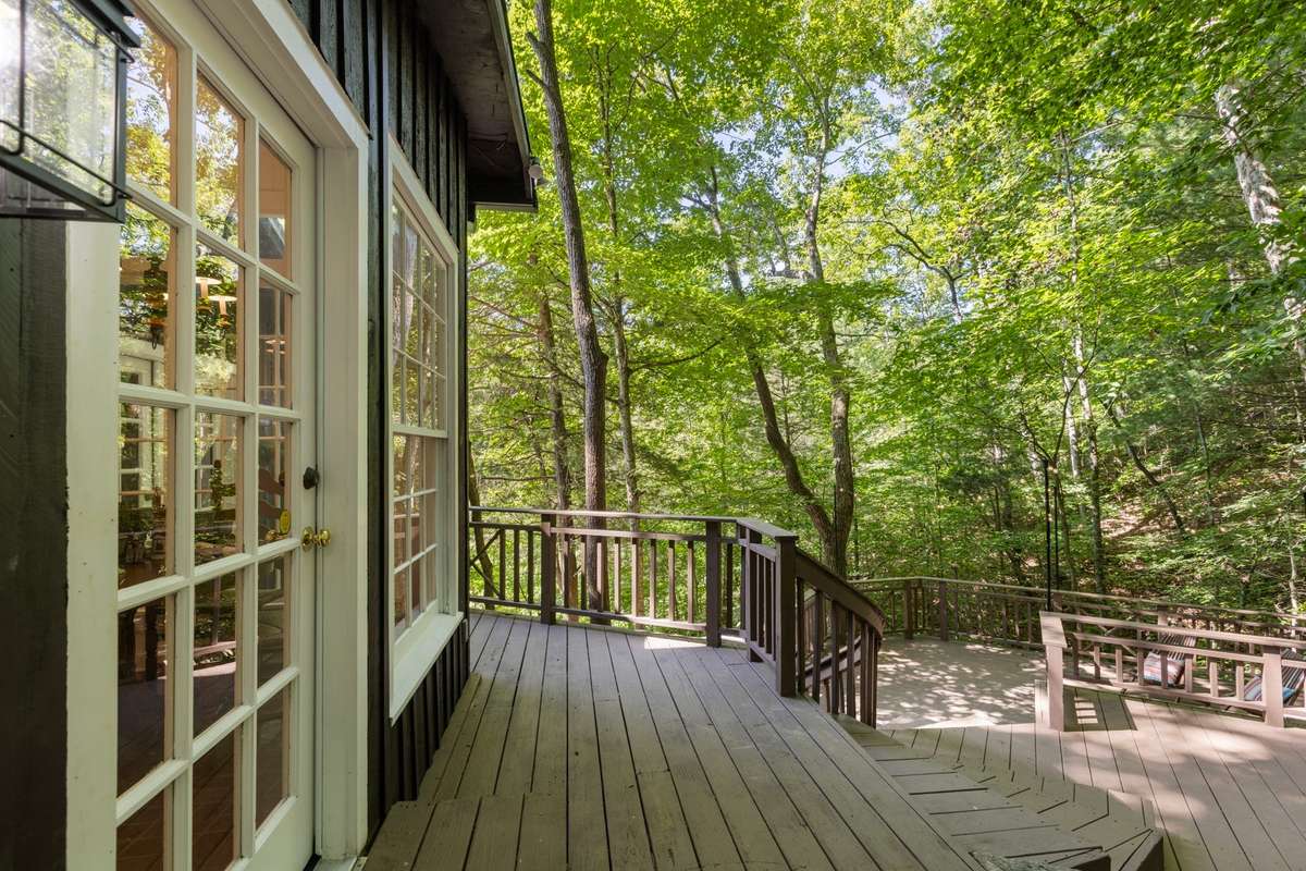 This view shows a spacious multi-tiered deck wrapping around the cabin creating a perfect setting for entertaining friends and family under a canopy of trees.