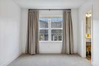 Close-up of the primary bedroom’s large window with custom blackout drapes, offering a bright view overlooking the private fenced back patio.