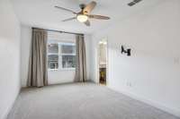 Spacious, light-filled primary bedroom featuring brand-new carpet throughout the entire upstairs level, a large window with custom blackout drapes, and access to a walk-in closet and en-suite bathroom.