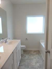 The primary bathroom comes with a two sink, soaking bath tub, shower, and an elongated toilet.
