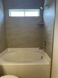 Tub shower combo with tile walls, tile floors and transom window for natural light