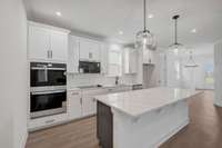 Chef's gourmet kitchen featuring built-in double wall ovens, quartz countertops, and ceramic tile backsplash. Dark gray island cabinets for a fun design pop!