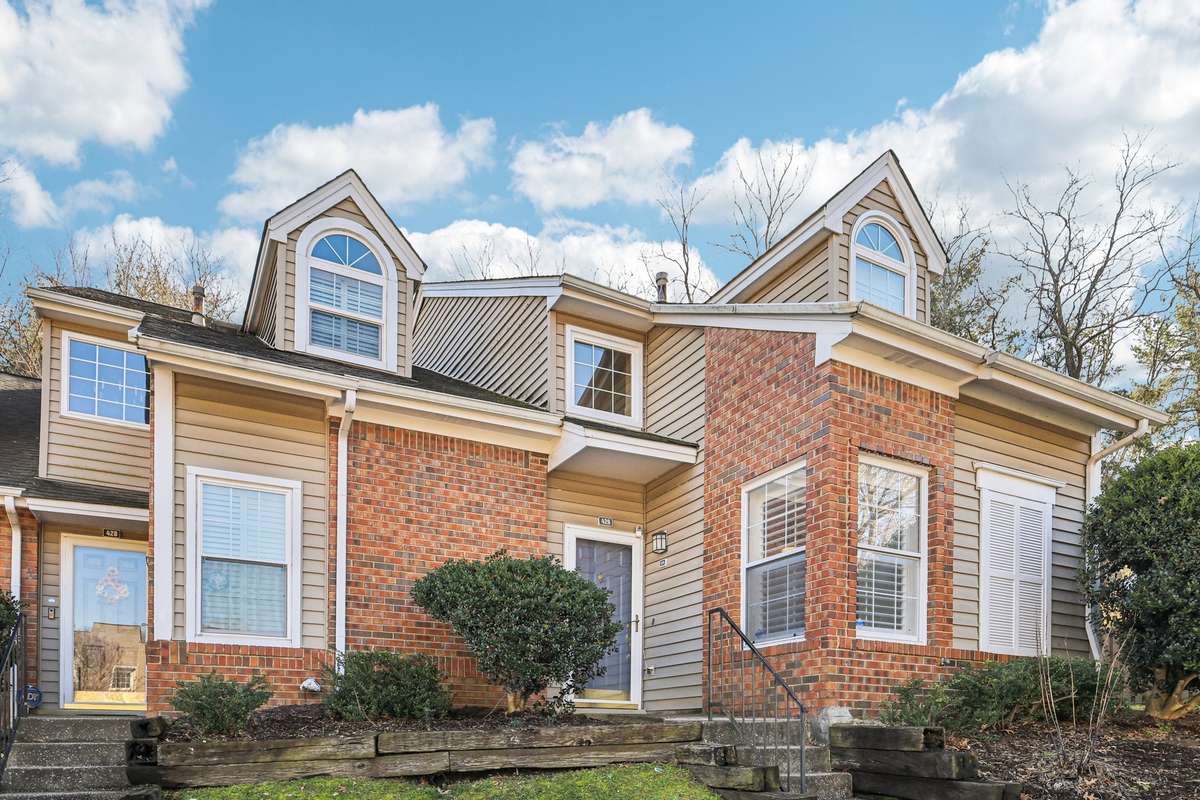 Charming curb appeal with classic brick and siding exterior, accented by arched dormer windows and white shutters. Front steps lead to a private entrance framed by mature landscaping.