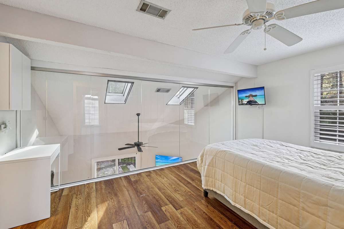 Stunning view from the lofted primary suite with dramatic vaulted ceilings, skylights, and a modern ceiling fan overlooking the living area below.