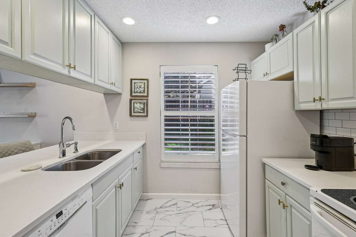 Bright and airy kitchen features white cabinetry, quartz counters, and a window with plantation shutters that allows natural light to flood the space.