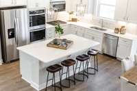 Gather around your oversized island with quartz overhang for barstool seating. In this community, your island will feature additional cabinetry not shown here.