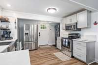 A beautifully upgraded kitchen featuring stainless steel appliances, open shelving, and warm wood flooring that ties the entire main level together.