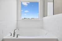 Unwind in your luxurious garden tub, surrounded by tile that adds a touch of sophistication. Perfect for relaxing, this tub offers a spa-like experience right at home, complemented by a picture window letting is natural light for a serene atmosphere.