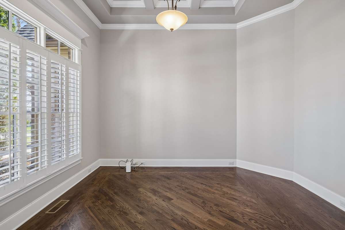 Large study with coffered ceiling accent and shutters look out to the front of the home.