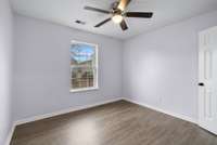 Bedroom three also features luxury vinyl flooring, a serene view overlooking the deck, a ceiling fan, and a full closet—making it a tranquil and stylish space for guests or family.