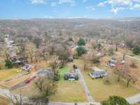 An Elevated aerial view showcasing the property’s setting and surrounding neighborhood, featuring a spacious lot with mature trees, and convenient road access. A great perspective of the home’s location, privacy, and the peaceful, established area.