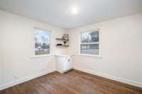 Light-filled dining room with warm hardwood floors, crisp neutral paint, and bright trim throughout. Two large windows bring in abundant natural light and offer pleasant outdoor views, creating an inviting space for everyday meals or entertaining.