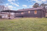 Rear view of the home showcasing a spacious backyard and a large covered carport/parking area for added convenience.