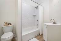 Updated bathroom in the finished studio space above the garage featuring a bright tub/shower combo with classic white subway tile surround and a sleek rain-style showerhead