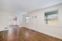 Bright and welcoming living space featuring freshly painted walls, large windows for abundant natural light, and beautiful hardwood floors that flow seamlessly into the adjoining dining area.