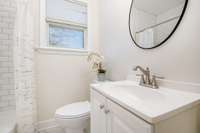 Fresh, bright Full Bath featuring a clean white vanity with brushed nickel fixtures, and a modern round mirror. The shower showcases classic white subway tile and a crisp, updated look.